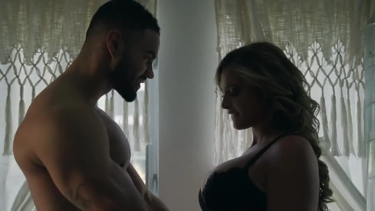 A man and a woman standing close together, both looking at each other with soft expressions.
