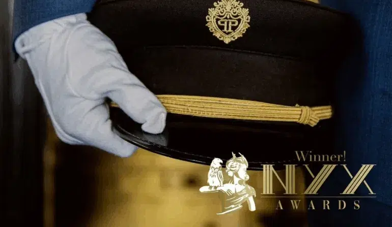 A hand in a white glove holding a military-style hat with gold trim and emblem. A hand in a white glove holding a military-style hat with gold trim and emblem.